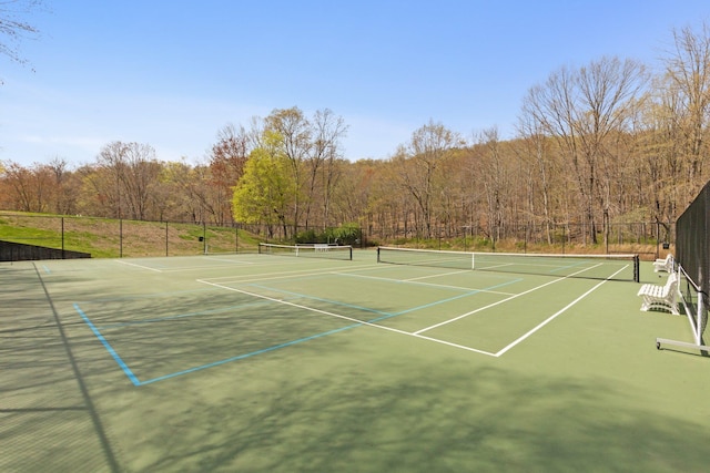 view of sport court with a wooded view, community basketball court, and fence