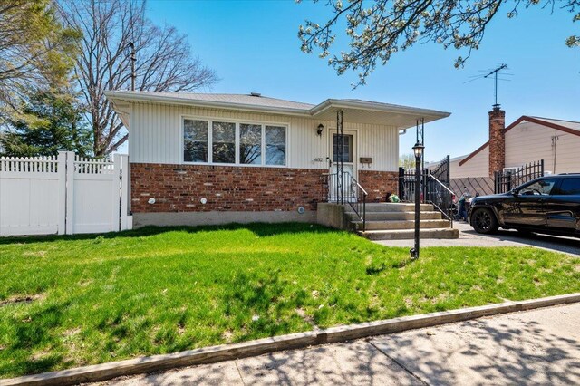 bungalow featuring fence, a front lawn, and brick siding