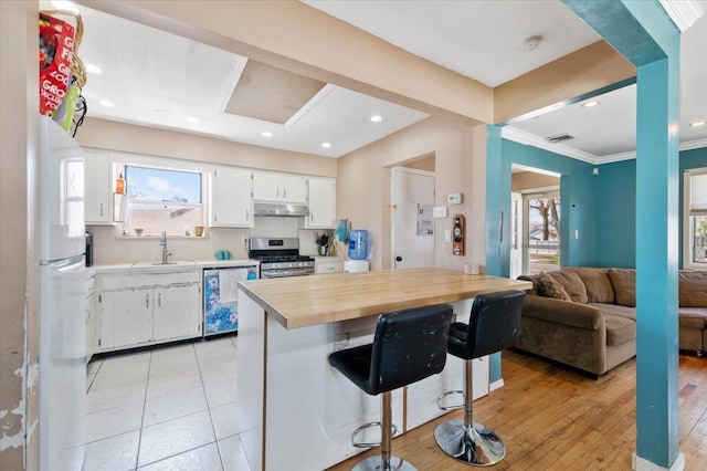 kitchen with stainless steel range with gas cooktop, white cabinetry, a breakfast bar, under cabinet range hood, and dishwashing machine