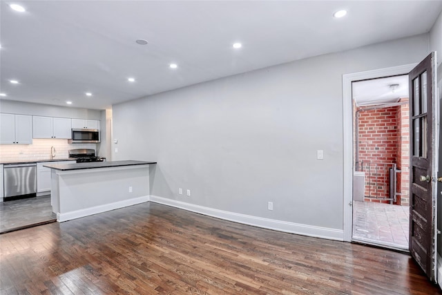kitchen featuring white cabinets, a sink, dark wood-style flooring, decorative backsplash, and appliances with stainless steel finishes