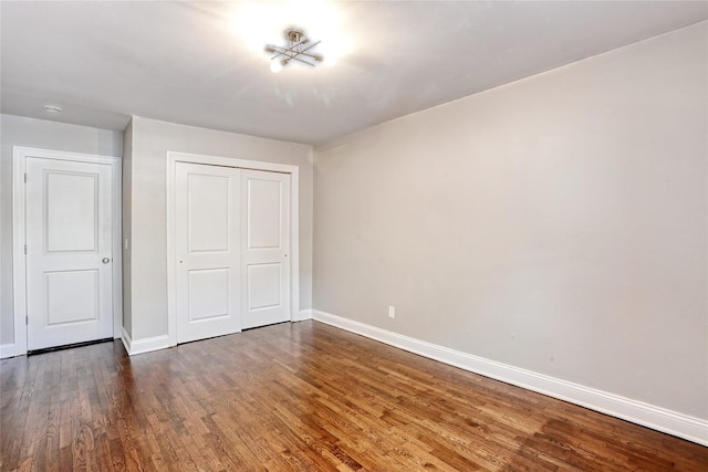 unfurnished bedroom with dark wood finished floors, baseboards, and a closet