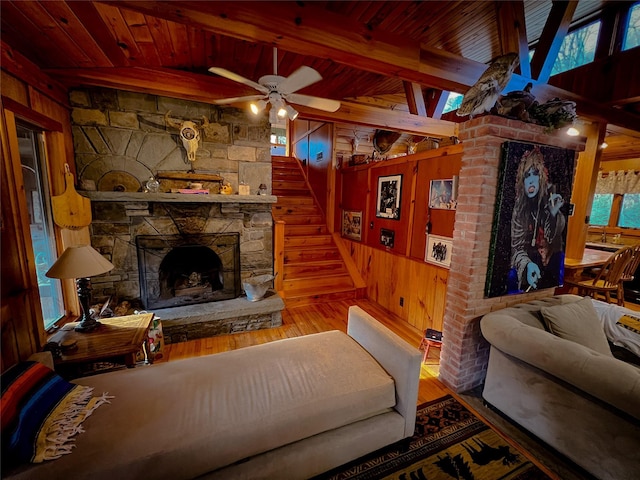 living room featuring hardwood / wood-style floors, wood walls, a stone fireplace, a ceiling fan, and wooden ceiling
