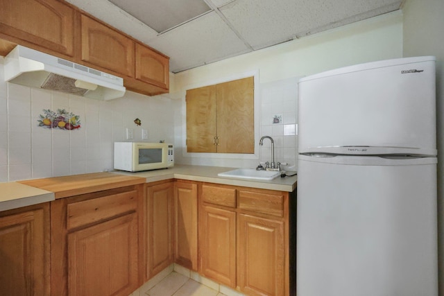 kitchen featuring tasteful backsplash, refrigerator, a sink, white microwave, and under cabinet range hood