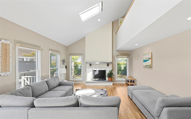 living area with high vaulted ceiling, a healthy amount of sunlight, light wood-style flooring, and a skylight