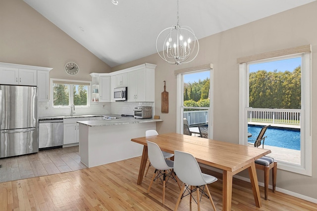 dining space featuring high vaulted ceiling, a notable chandelier, a toaster, and light wood-style flooring