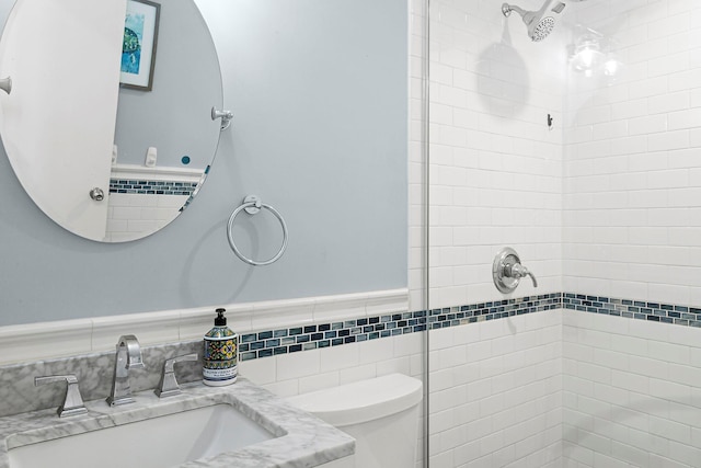 bathroom with a tile shower, toilet, and a sink
