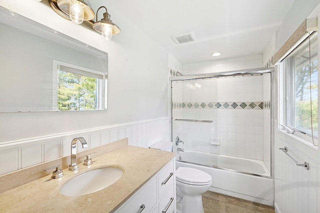 bathroom featuring a wainscoted wall, visible vents, toilet, vanity, and bath / shower combo with glass door