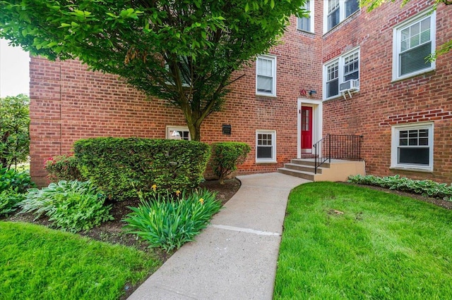 entrance to property with brick siding, a lawn, and cooling unit