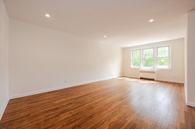 empty room featuring radiator heating unit, wood finished floors, baseboards, and recessed lighting