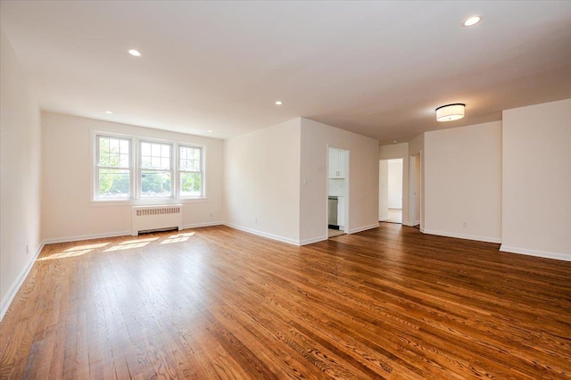 empty room with radiator, wood finished floors, baseboards, and recessed lighting