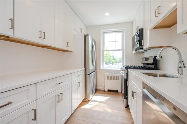 kitchen with stainless steel appliances, a sink, radiator, white cabinets, and light wood-style flooring