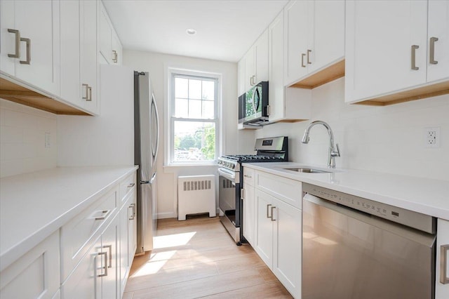 kitchen featuring stainless steel appliances, a sink, radiator, tasteful backsplash, and light wood finished floors