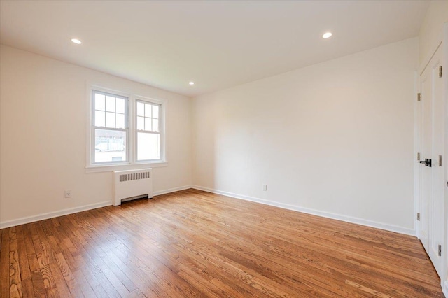unfurnished room featuring radiator, light wood-style flooring, baseboards, and recessed lighting