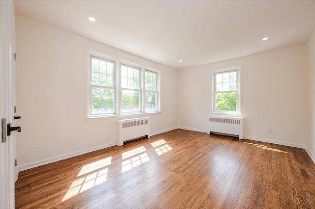 unfurnished room with radiator, wood finished floors, baseboards, and recessed lighting