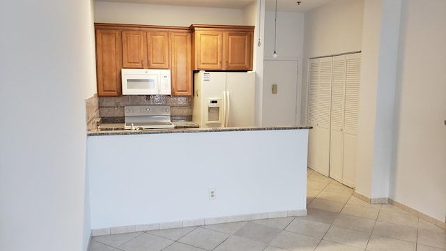 kitchen with dark stone countertops, light tile patterned floors, white appliances, decorative backsplash, and a peninsula