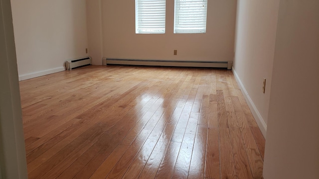 empty room featuring baseboard heating, light wood-type flooring, a baseboard heating unit, and baseboards