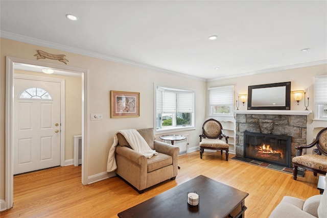 living room featuring a stone fireplace, light wood finished floors, baseboards, and ornamental molding