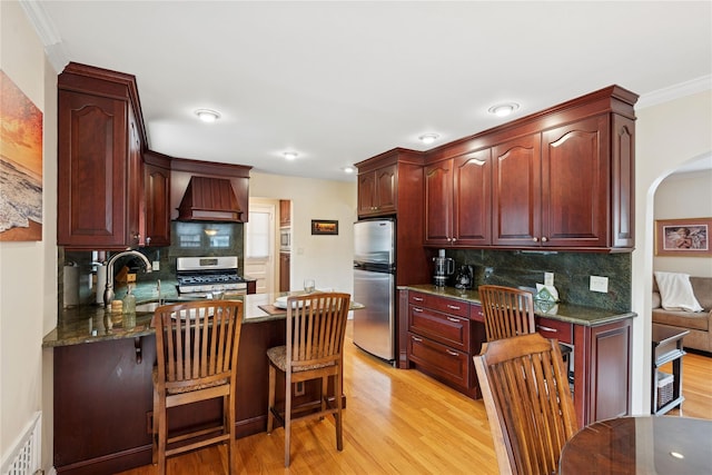 kitchen featuring premium range hood, light wood-type flooring, stainless steel appliances, and a sink