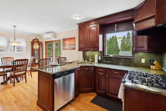 kitchen featuring light wood finished floors, a wall unit AC, a sink, a peninsula, and appliances with stainless steel finishes