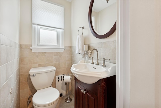 half bath featuring tile walls, toilet, vanity, and wainscoting