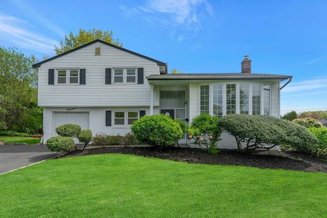 split level home with a chimney, a front lawn, a garage, asphalt driveway, and brick siding