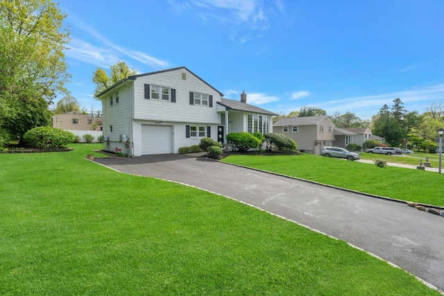split level home featuring driveway, an attached garage, a chimney, and a front lawn