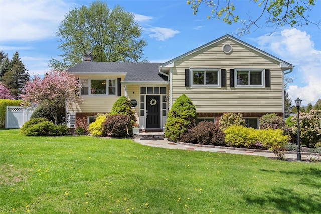 view of front of property featuring brick siding, a front lawn, fence, and a chimney