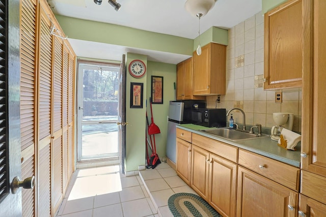 kitchen with backsplash, black microwave, a sink, light tile patterned floors, and freestanding refrigerator