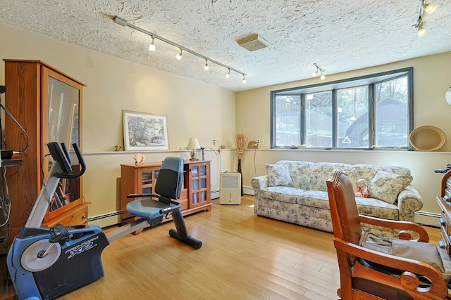 exercise area featuring a textured ceiling, track lighting, baseboard heating, and wood finished floors
