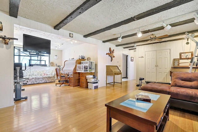 living room featuring a textured ceiling, wood finished floors, track lighting, beamed ceiling, and wooden walls
