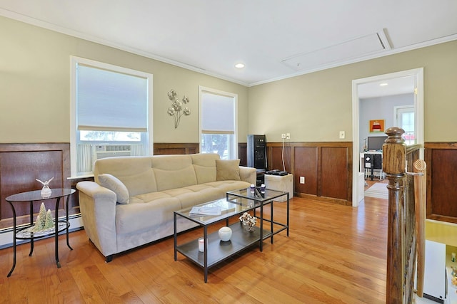 living room with crown molding, wainscoting, baseboard heating, attic access, and light wood-type flooring