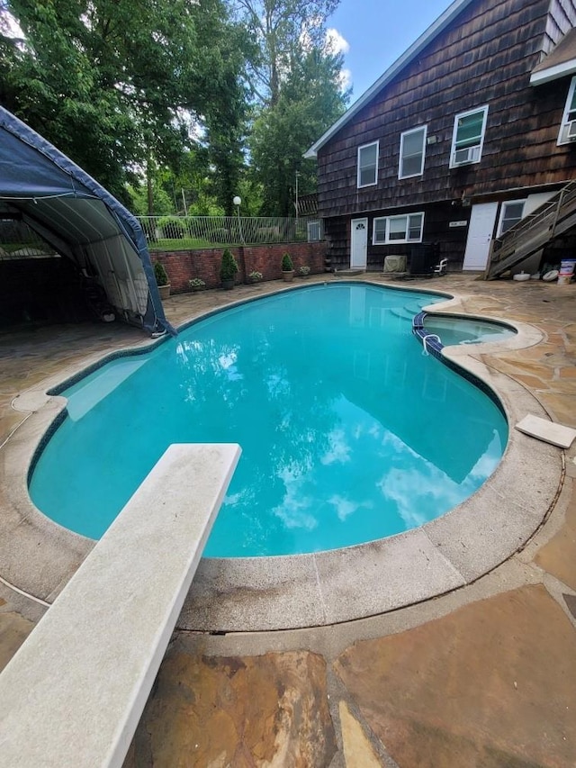 view of swimming pool with a diving board, a pool with connected hot tub, fence, and a patio area