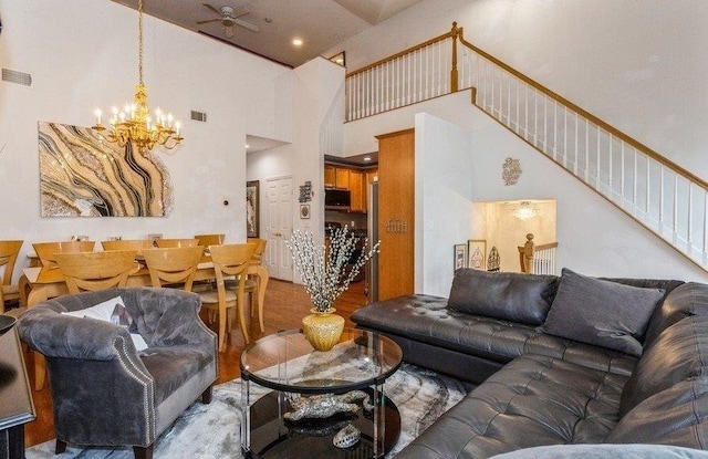 living area with visible vents, a high ceiling, stairs, and ceiling fan with notable chandelier