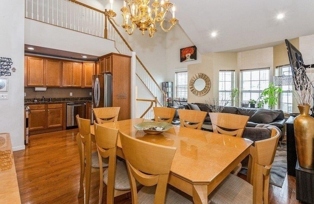 dining space featuring stairway, wood finished floors, an inviting chandelier, a towering ceiling, and recessed lighting