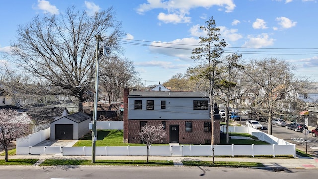 view of front of property featuring a fenced front yard, an outdoor structure, brick siding, a front yard, and a garage