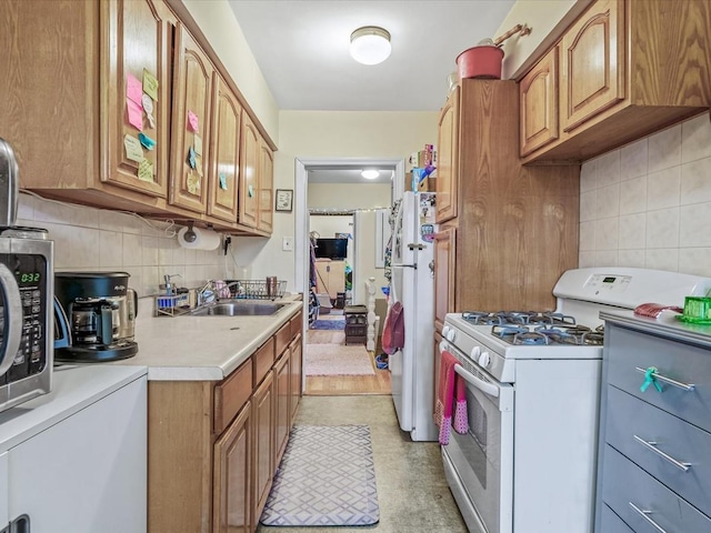 kitchen with decorative backsplash, light countertops, white appliances, and a sink