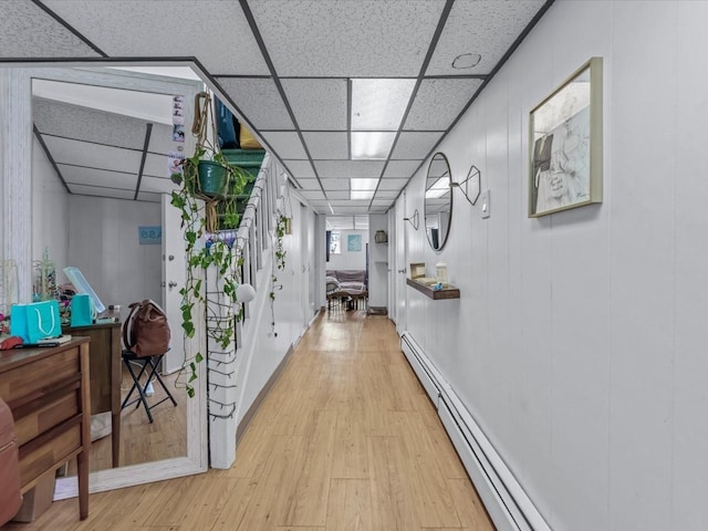 hallway with a baseboard heating unit, wood finished floors, and a drop ceiling