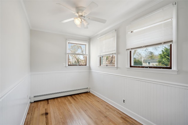 spare room with light wood-style flooring, wainscoting, baseboard heating, a ceiling fan, and ornamental molding