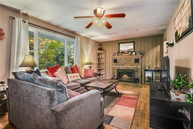 living area featuring a glass covered fireplace, wood finished floors, wooden walls, and ceiling fan