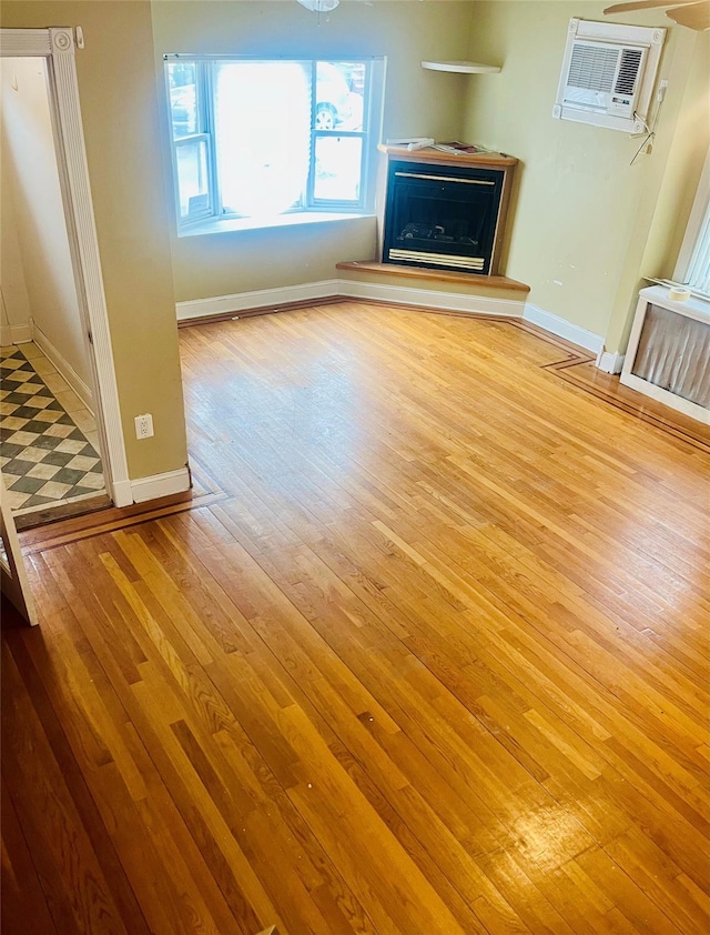 93-30 246th St, Bellerose Terrace, NY 11001 - unfurnished living room featuring hardwood / wood-style floors, baseboards, a fireplace with raised hearth, and a wall mounted air conditioner