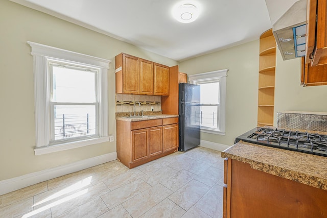 kitchen with a sink, tasteful backsplash, baseboards, freestanding refrigerator, and brown cabinetry