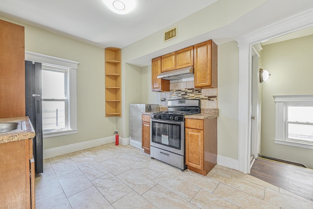 kitchen featuring under cabinet range hood, light countertops, stainless steel range with gas stovetop, visible vents, and tasteful backsplash