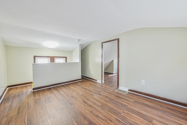 spare room with lofted ceiling, baseboards, wood finished floors, and visible vents