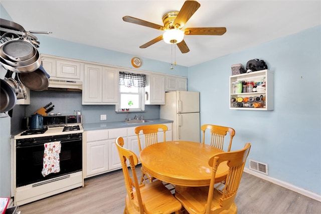 kitchen featuring range with gas cooktop, a sink, under cabinet range hood, visible vents, and freestanding refrigerator