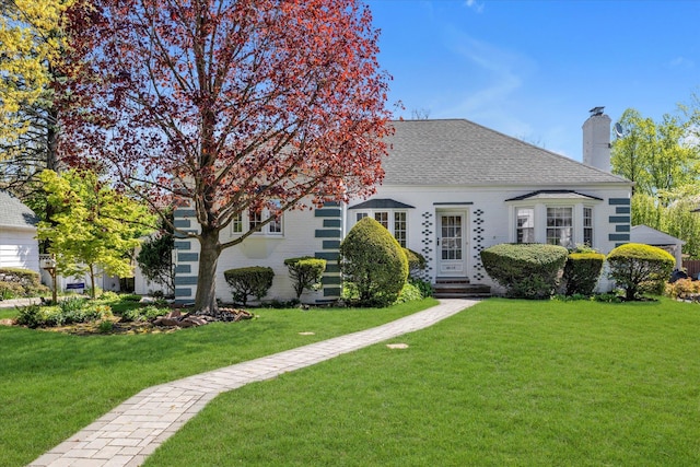 view of front of house with a shingled roof, a chimney, brick siding, and a front yard