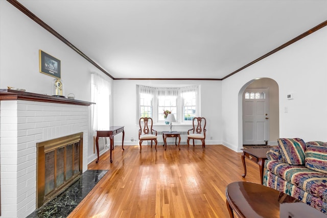 living area with crown molding, arched walkways, and light wood finished floors