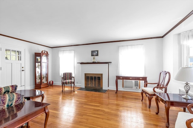 living room featuring a fireplace, baseboards, an AC wall unit, ornamental molding, and light wood-style flooring