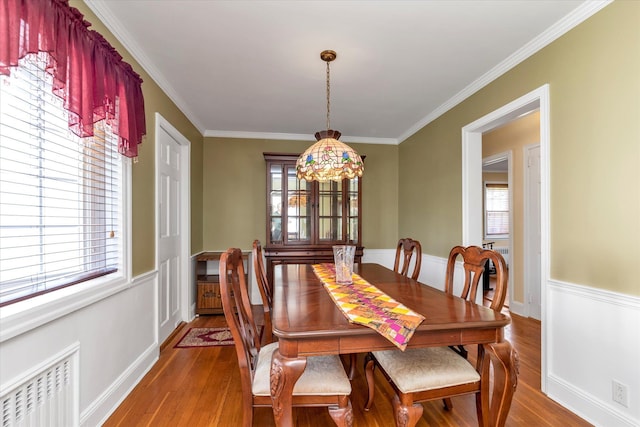 dining space featuring radiator heating unit, a wainscoted wall, ornamental molding, and wood finished floors
