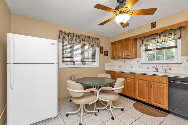 kitchen featuring decorative backsplash, a sink, light countertops, freestanding refrigerator, and black dishwasher
