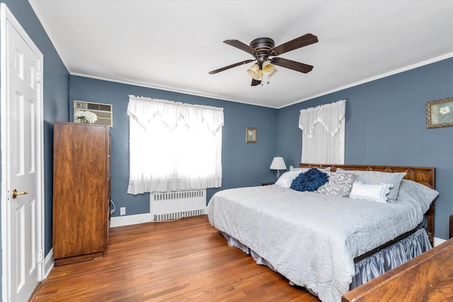 bedroom featuring ceiling fan, crown molding, wood finished floors, baseboards, and radiator heating unit